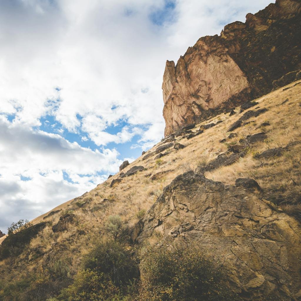 Spectacular scenery of high rocky hills covered with dry grass under cloudy blue sky in daytime